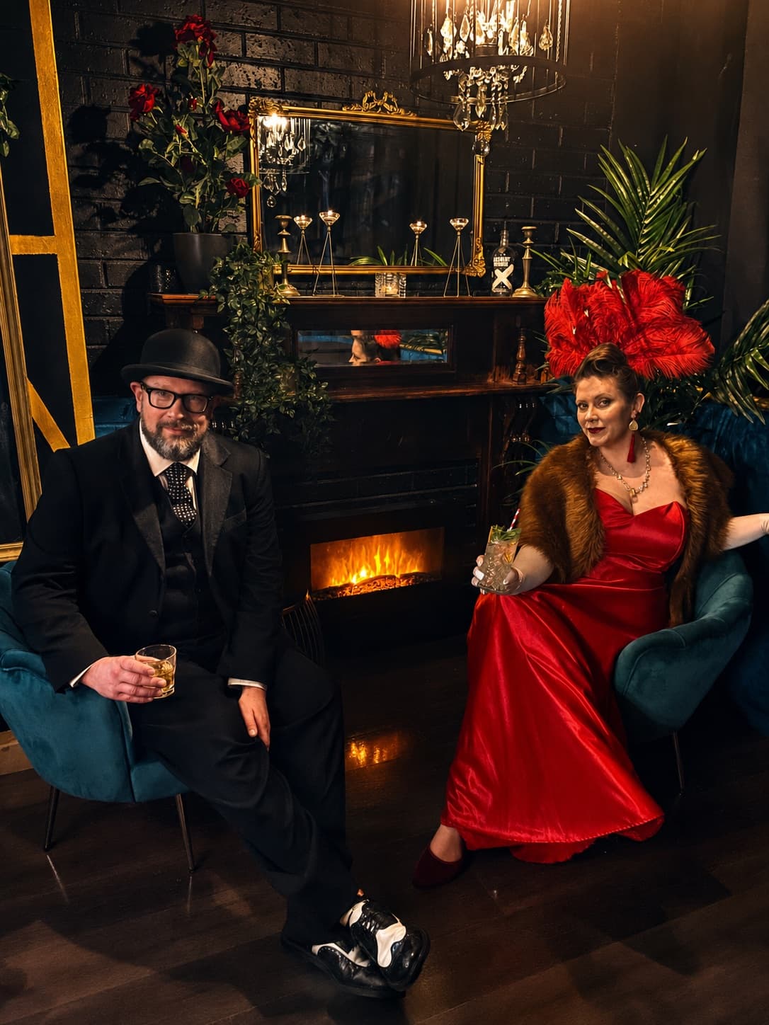 Two guests in evening dress with cocktails, seated by the fireplace and gold mirror in the Cocktail Lounge